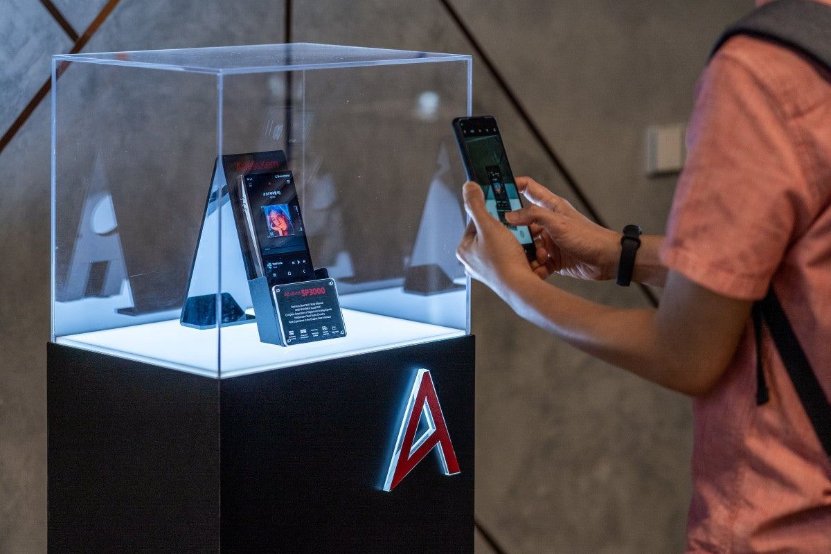 An individual using a smartphone to take photo of the Astell&Kern A&ultima SP3000 that is on display in an acrylic lightbox.