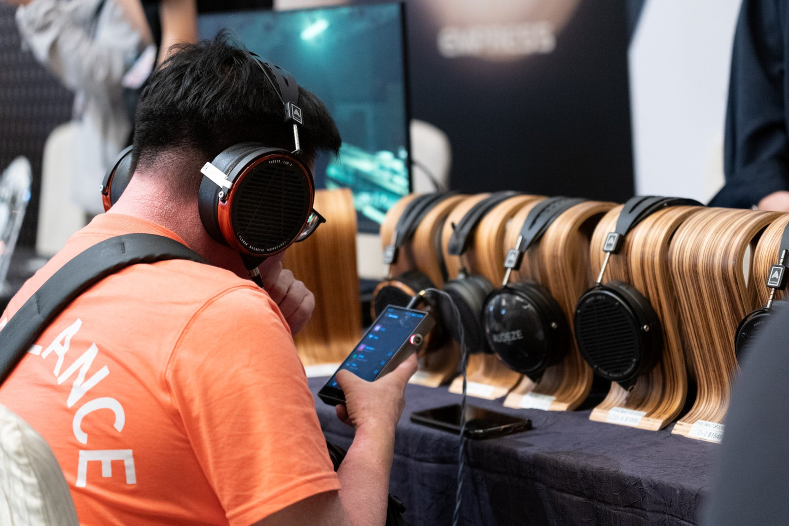 An attendee auditioning a pair of Audeze headphones with a row of other headphones on display in front of him.