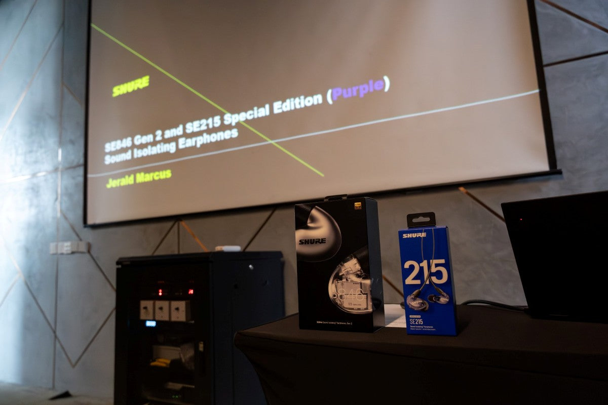 A photo of the packaging of the Shure SE846 Gen 2 and SE215 Special Edition Purple in the foreground with the presentation screen in the background.