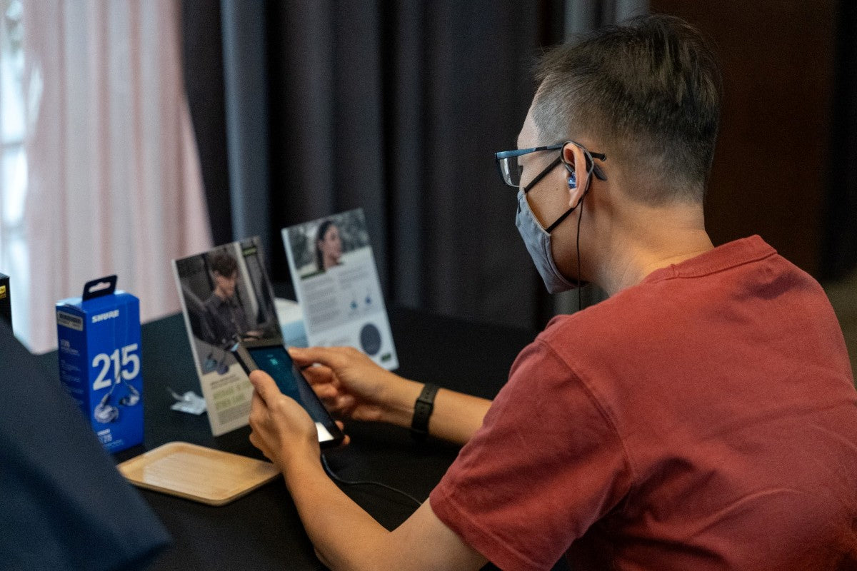 A man auditioning the Shure SE215 Special Edition Purple in-ear monitors while holding a digital audio player.